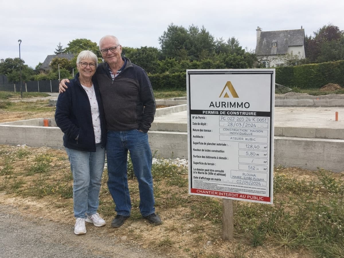 Anne-Marie et René devant leur chantier avec leur panneau de permis de construire Aurimmo