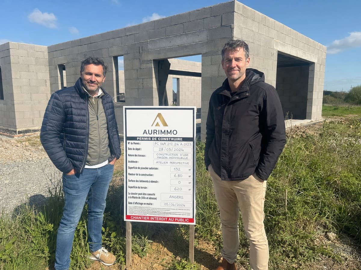 Arnaud et Esteban devant leur chantier avec leur panneau de permis de construire Aurimmo
